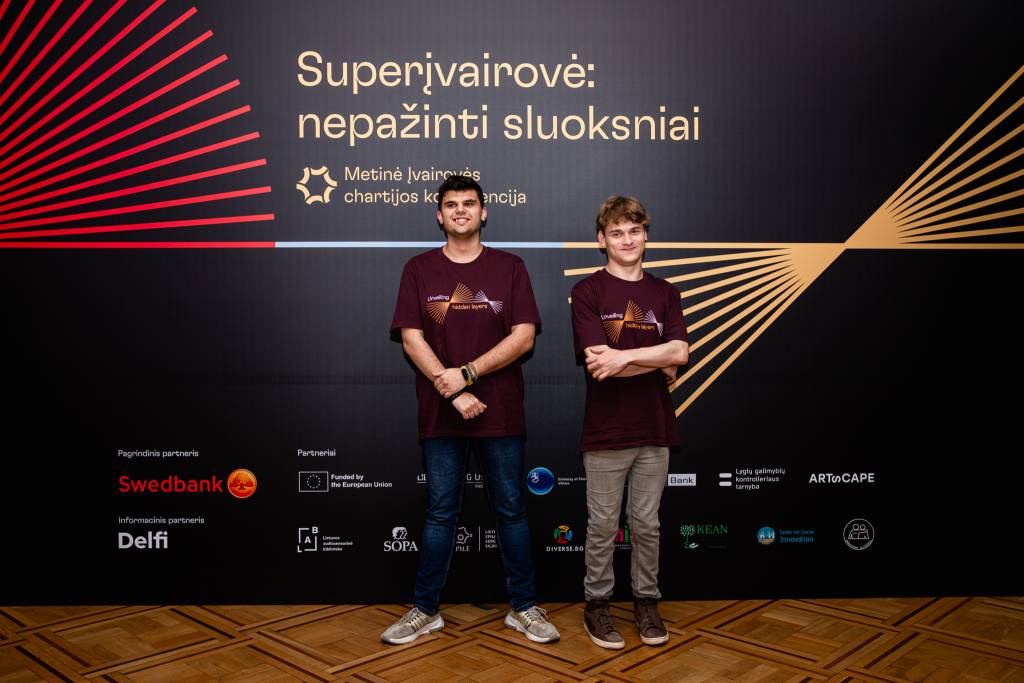 Arnas su draugu prie konferencijai skirto stendo ant kurio užrašyta: superįvairovė: nepažinti sluoksniai.